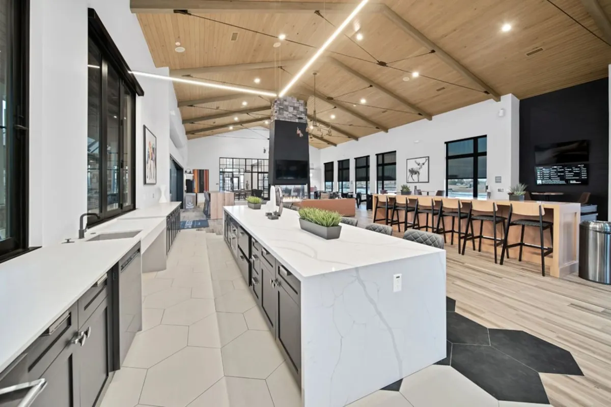An expansive kitchen and dining area with a large kitchen island, high ceilings, and a seamless flow into the adjacent dining space. The stainless steel appliances are complemented by a cozy fireplace and modern lighting, while the open layout encourages social gatherings and culinary creativity.