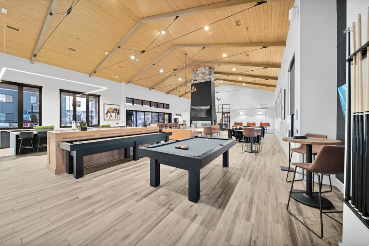 A lively interior lounge with a pool table, comfortable lounge seating, a fireplace, and large windows that bring in natural light. The space is suited for social gatherings, game nights, and casual relaxation.