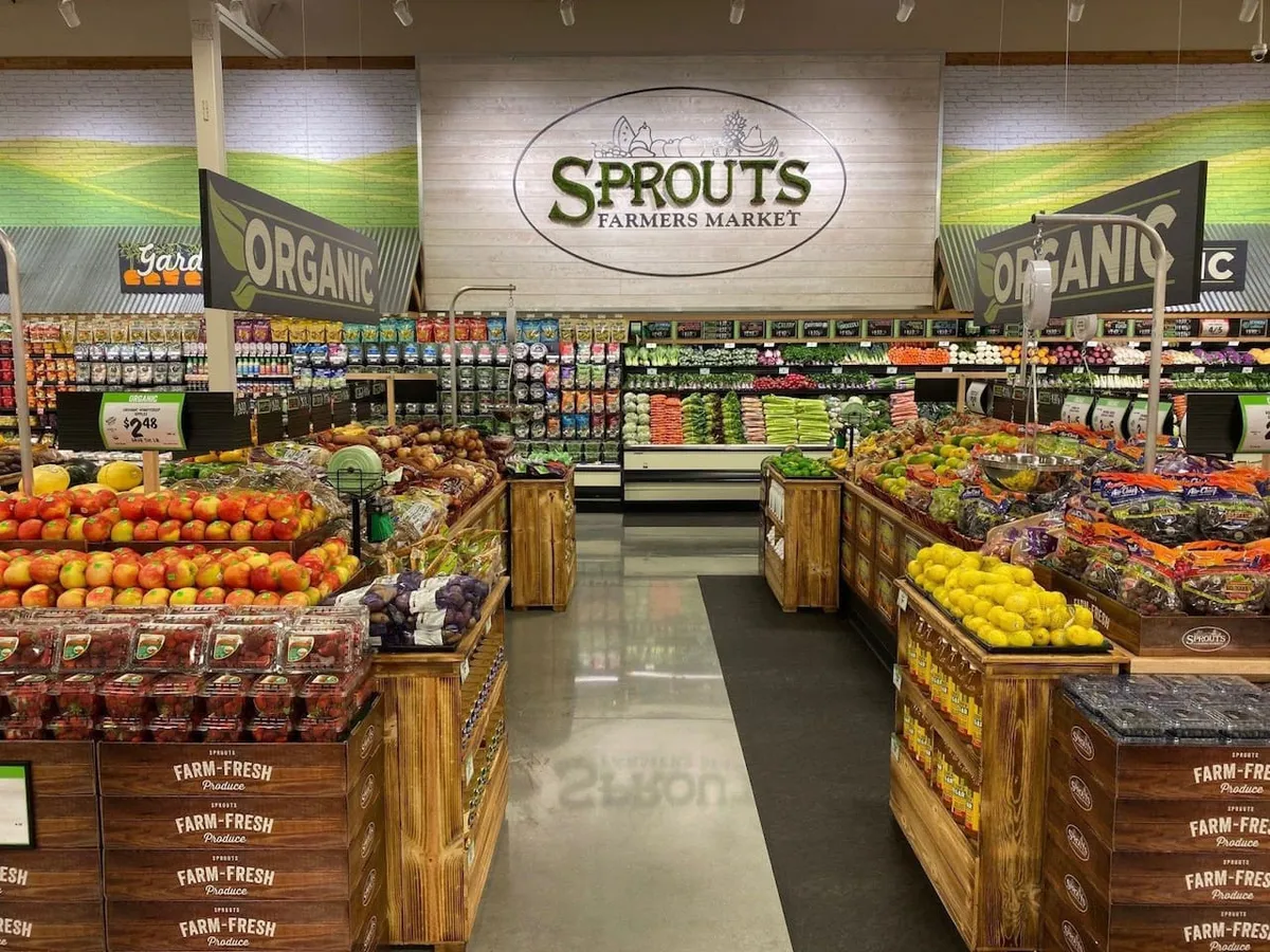 A colorful interior shot of a local Farmers Market with displays of fresh produce, organic signage, and engaging branding. Shoppers interact with the displays, highlighting the community’s health-conscious and social culture.