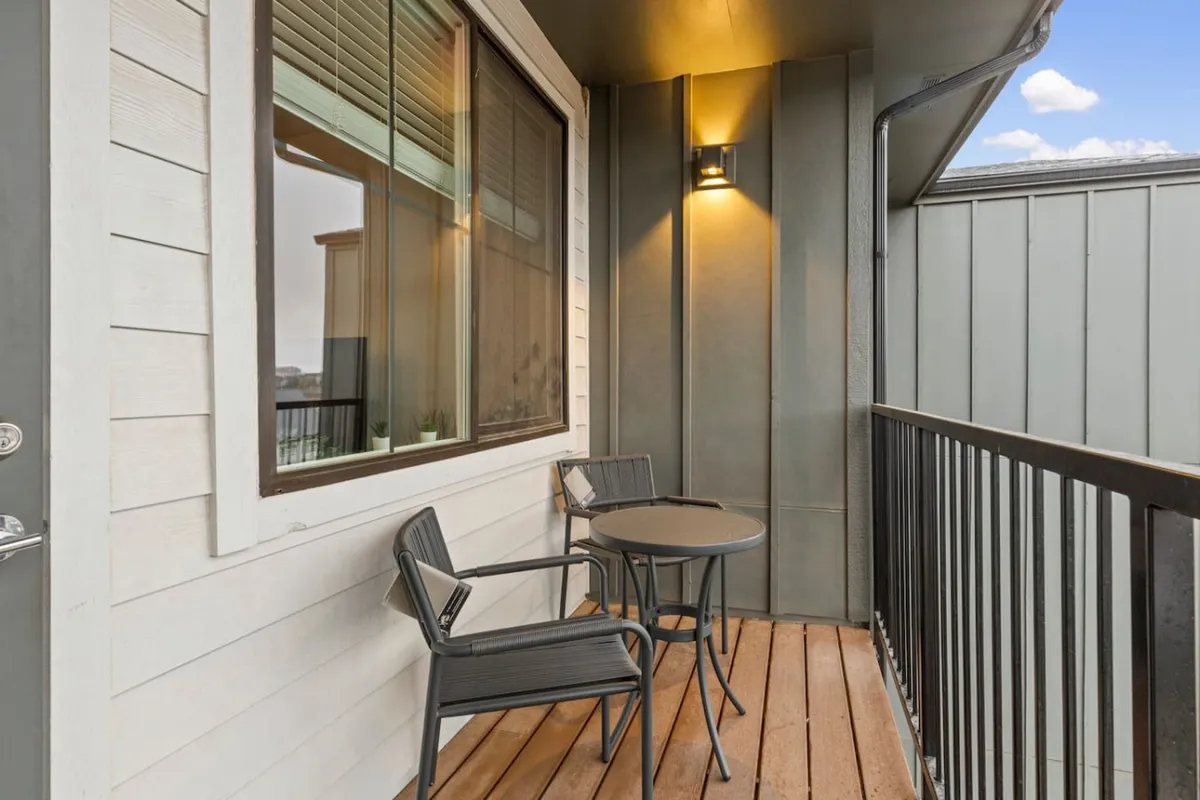 An inviting outdoor patio area with a table and chairs positioned beside a window. The setting suggests a peaceful spot for enjoying coffee at sunrise or unwinding with a glass of wine at sunset.
