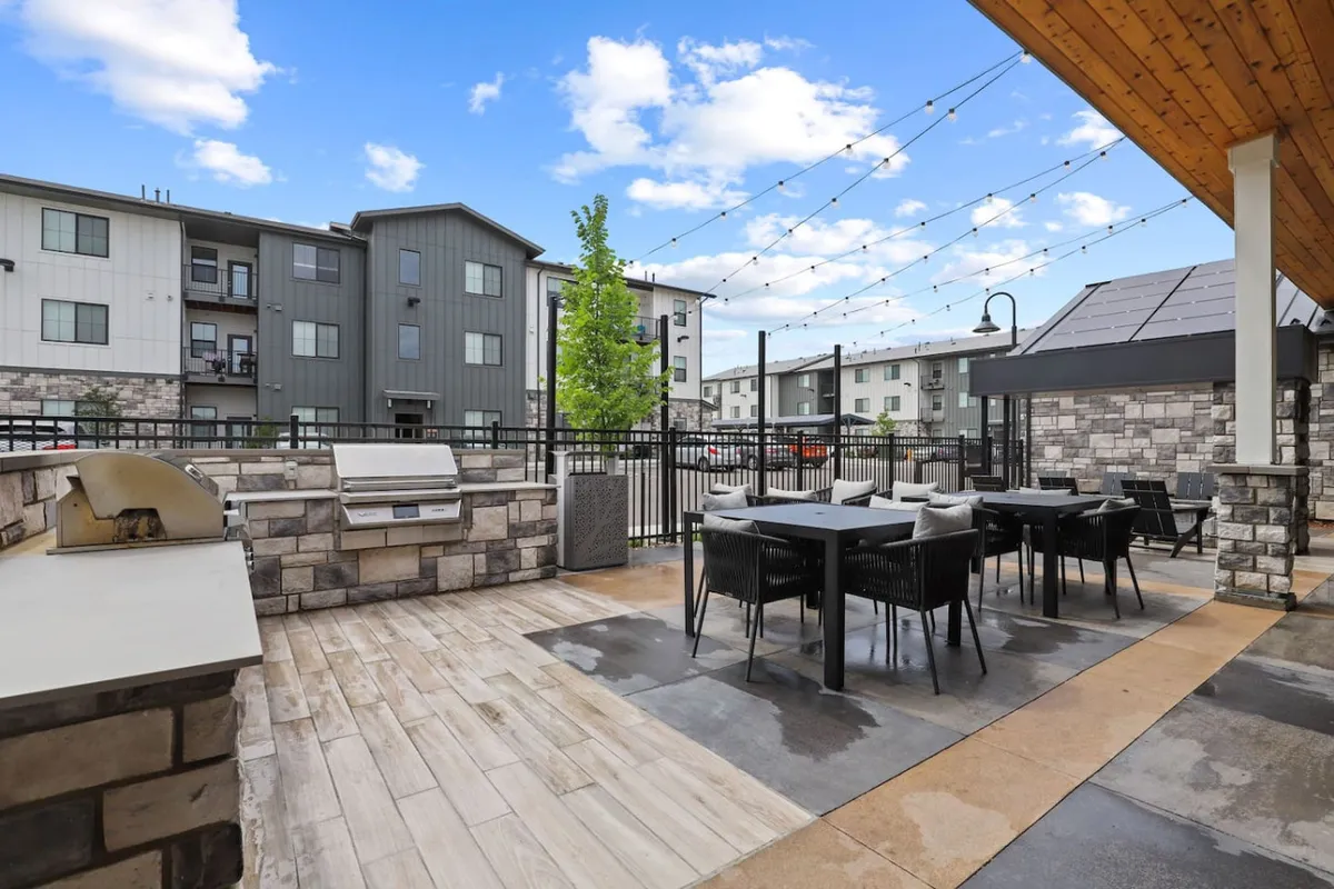 An inviting outdoor dining and grill area with a modern grill station, string lights, and a lush tree providing a cozy backdrop. The space is set up for communal barbecues, sunset dinners, and festive gatherings, showcasing the social and casual vibe of the community.