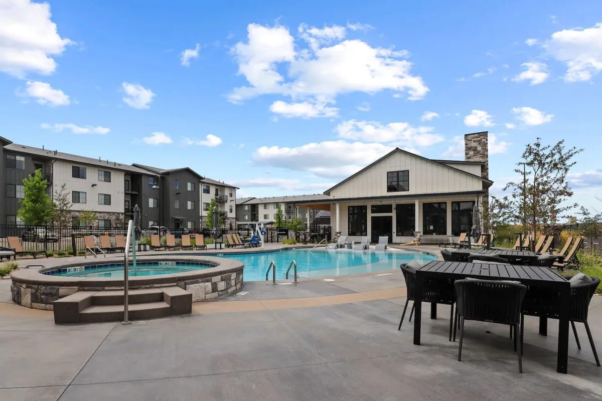 A vibrant exterior scene featuring a sparkling swimming pool and hot tub surrounded by lounge chairs and an outdoor clubhouse. The area is lively and social, with space for swimming, sunbathing, and gathering with neighbors. Outdoor seating and barbecue amenities are visible, emphasizing communal leisure.