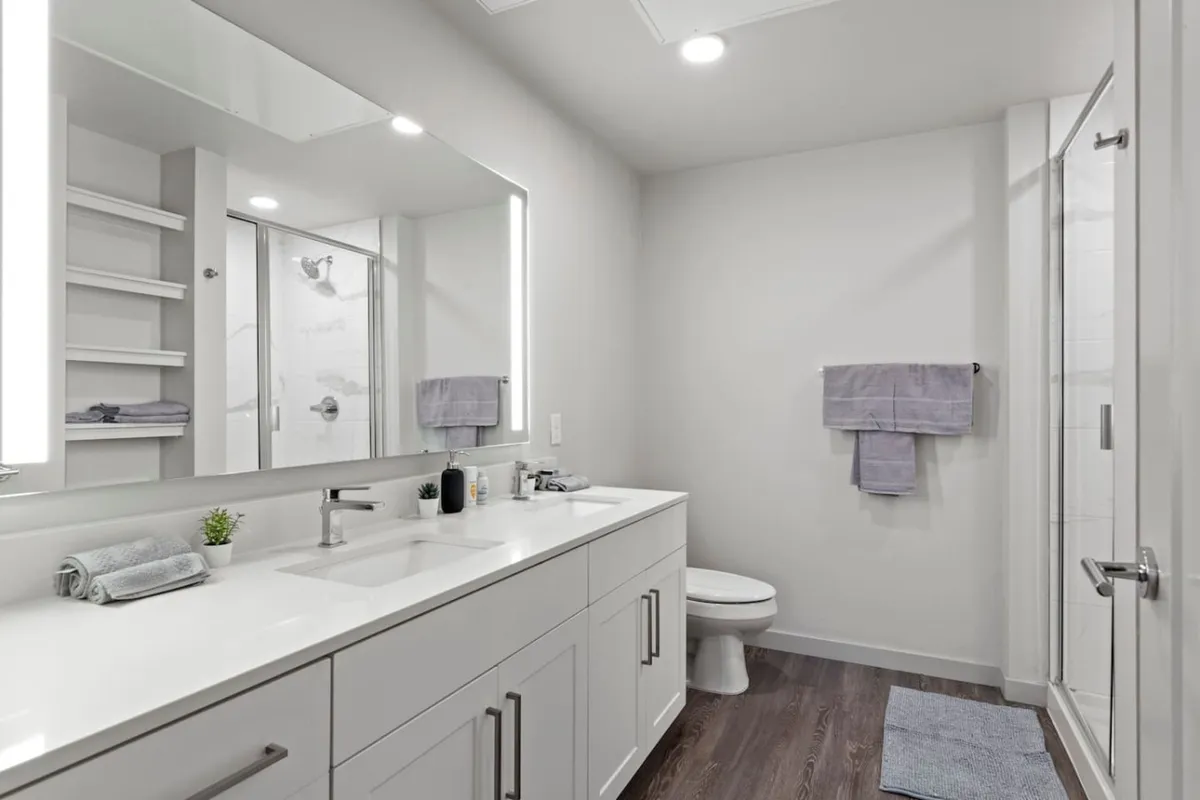 A spacious bathroom with a double sink vanity, large mirrors, a shower enclosure, fresh towels, and a small plant. The space feels modern, serene, and thoughtfully organized, ideal for rejuvenating personal routines.