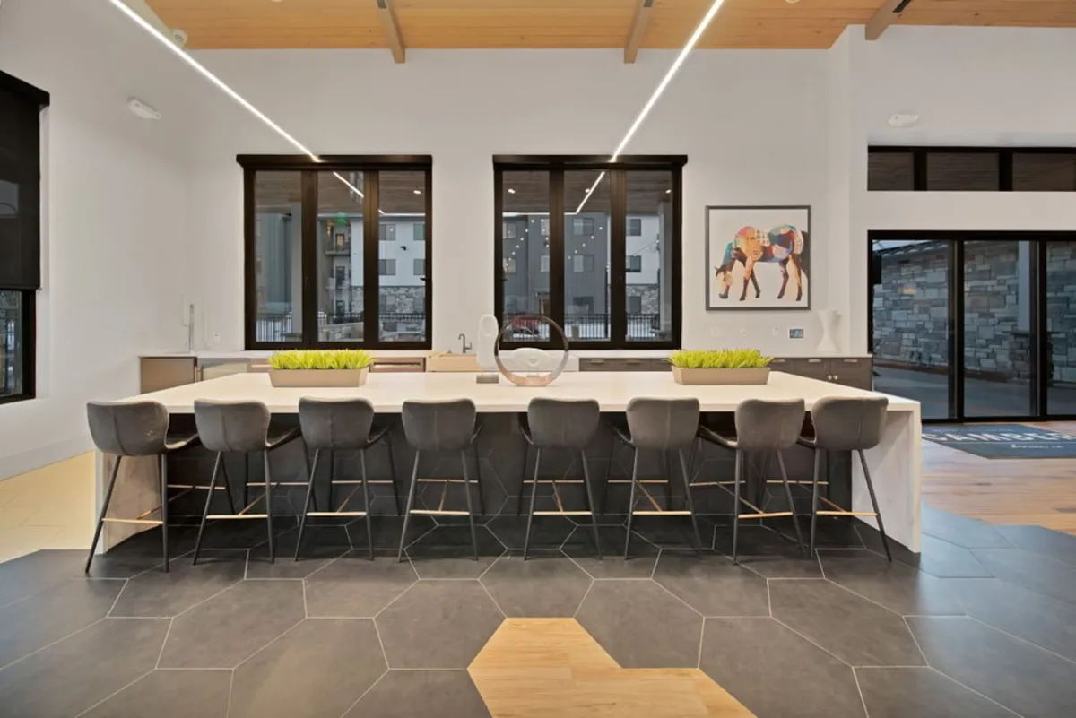 A bright kitchen anchored by a large central island, surrounded by hexagonal floor tiles, with natural light streaming through windows and modern wall art adding a splash of color. The space feels ready for gatherings, informal meals, or culinary experiments.