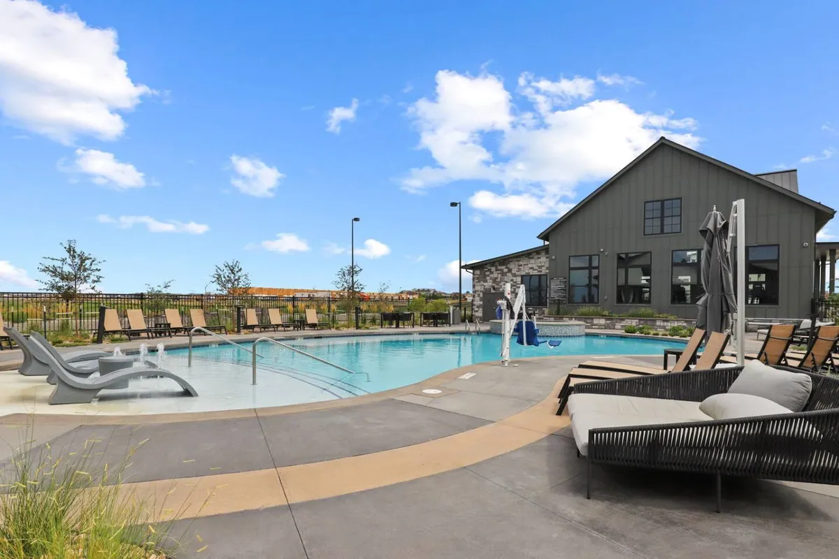 An inviting exterior view of the resort-style swimming pool surrounded by lounge chairs and lush landscaping, with the community clubhouse in the background. The tranquil atmosphere suggests opportunities for relaxation and social gatherings, especially at sunset.